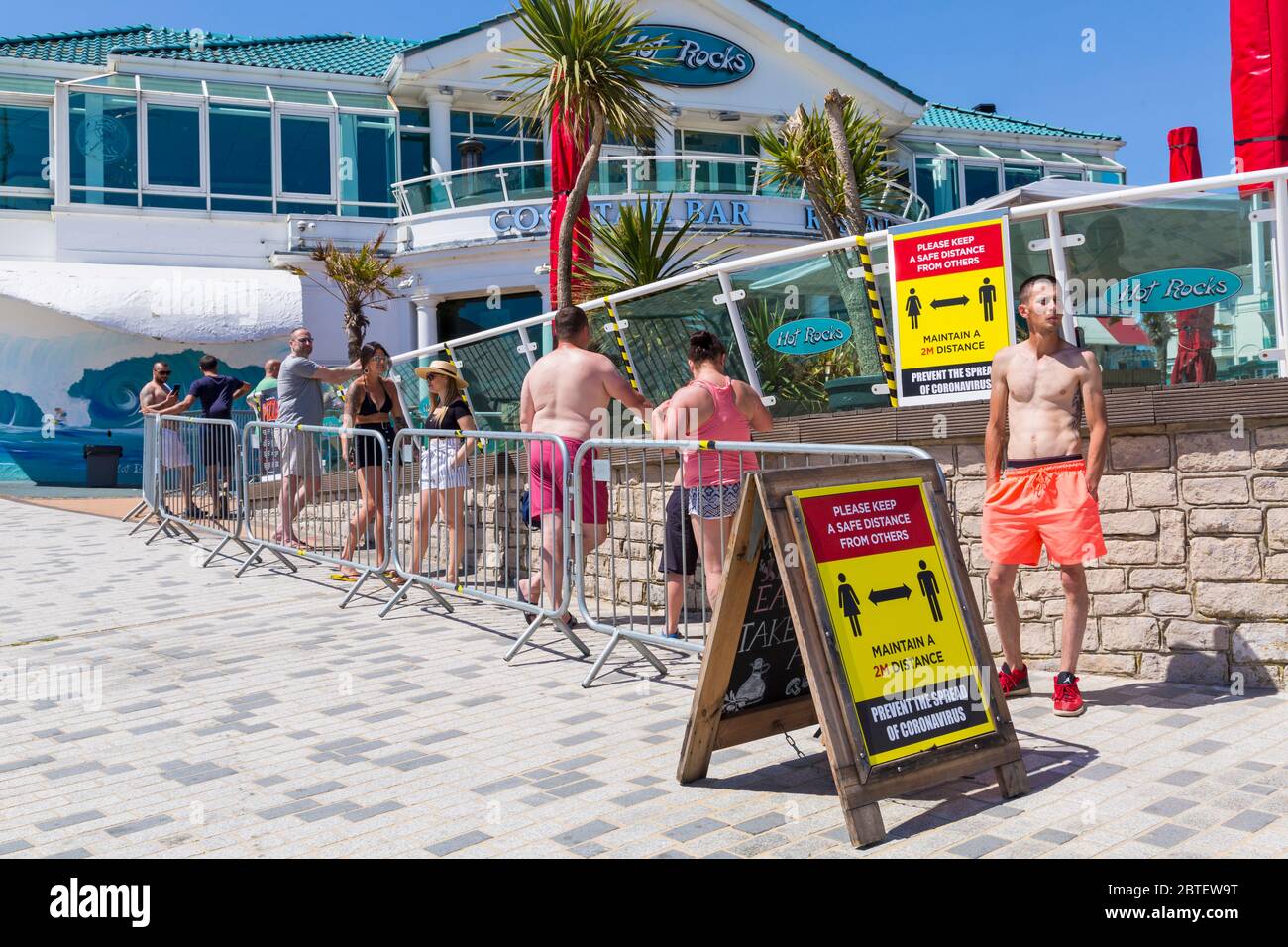 Bournemouth, Dorset UK. 25th May 2020. Social distancing as visitors queue for drinks and take away pizzas at Hot Rocks on a scorching hot day at Bournemouth beaches with clear blue skies and unbroken sunshine, as temperatures soar on Bank Holiday Monday. Sunseekers flock to the seaside and beaches are packed. Credit: Carolyn Jenkins/Alamy Live News Stock Photo
