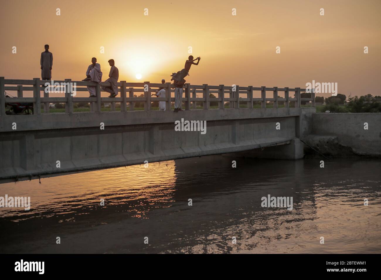 Kids Sitting Water From A Bridge During Sunset, In Moro, Sindh, Pakistan 26/08/2017 Stock Photo