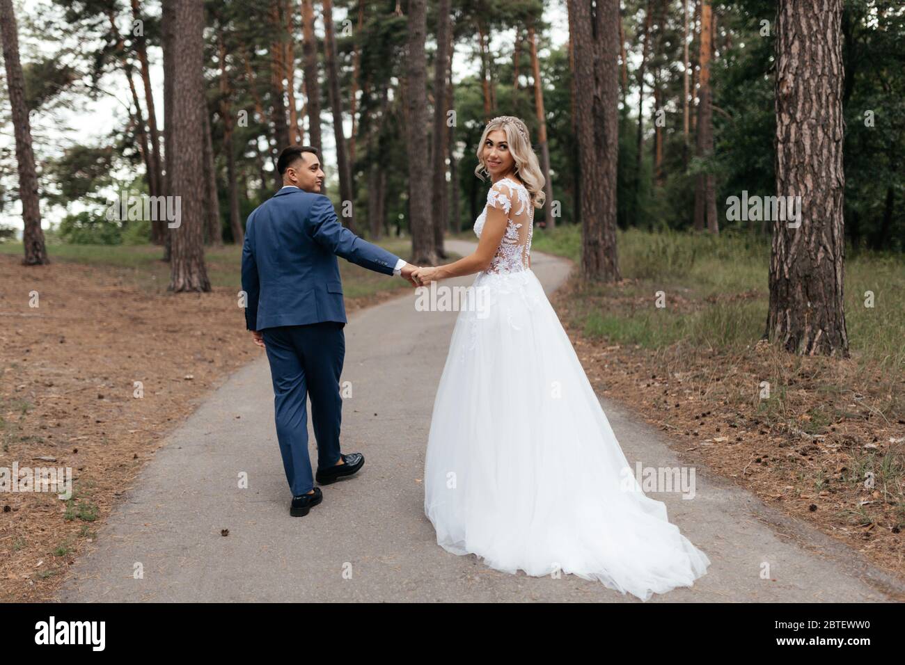 Bride and groom walking in the park holding hands photographed from the ...