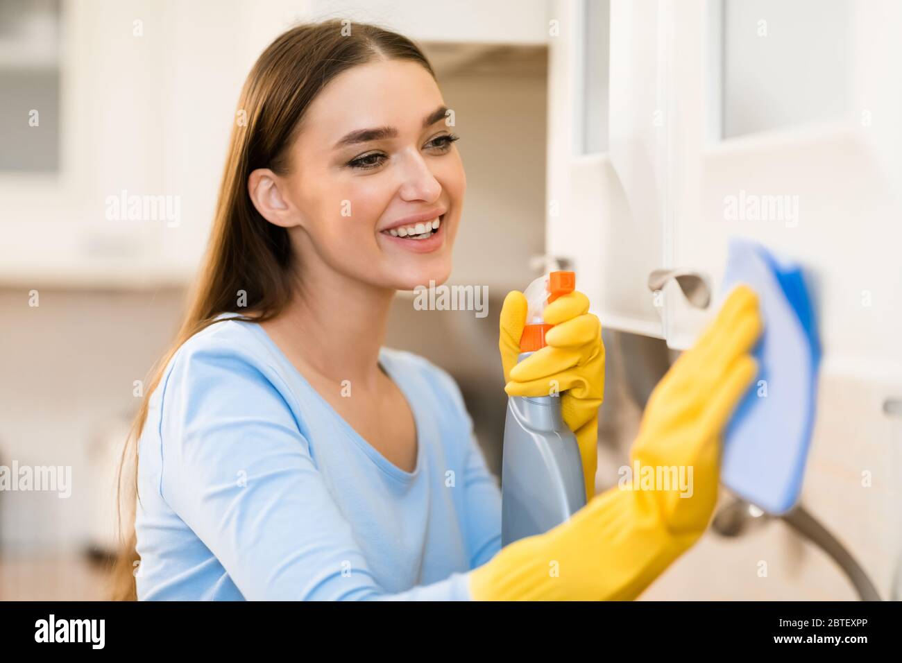 Young woman cleaning kitchen furniture using cloth and spray Stock Photo