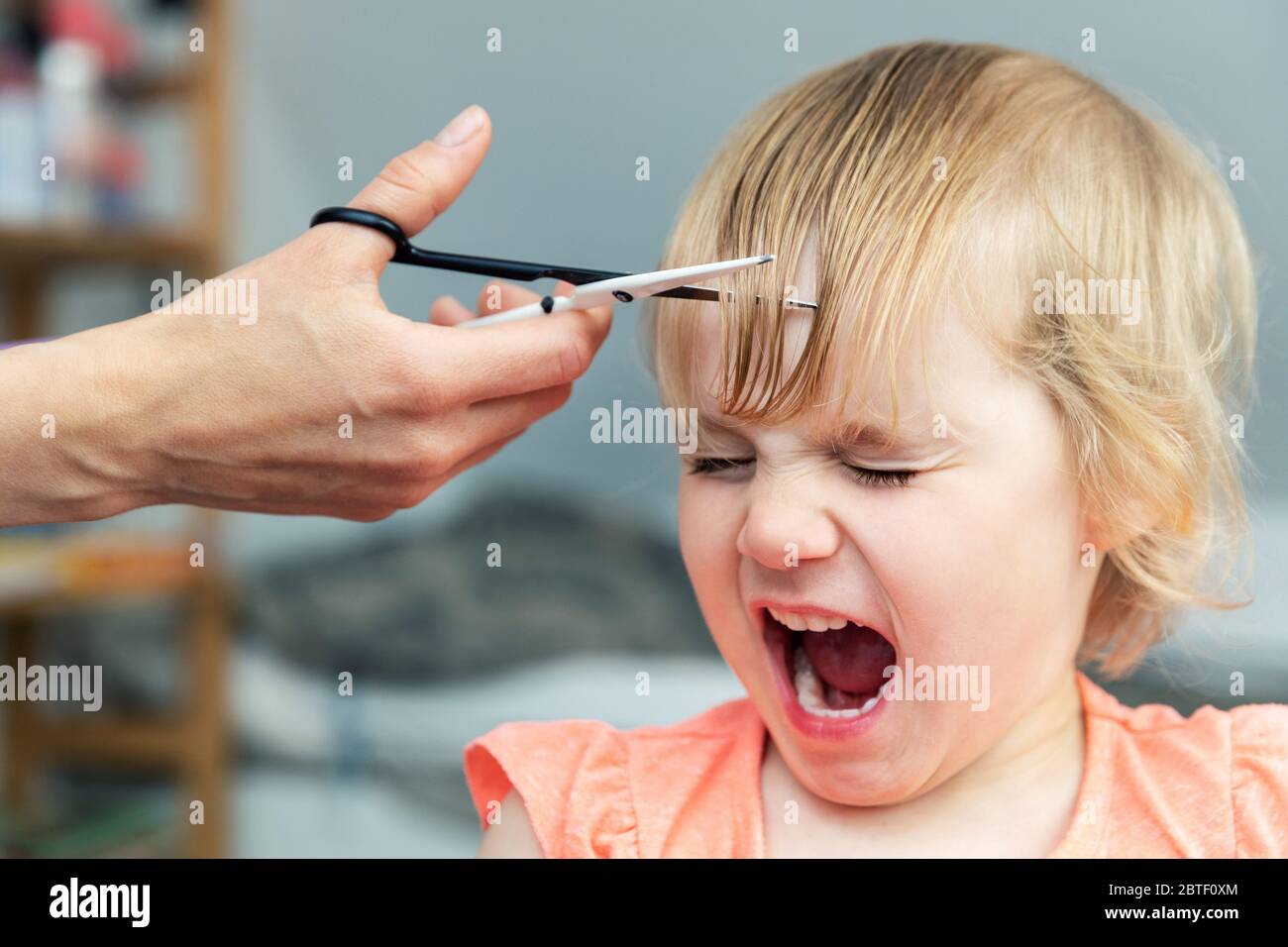 little girl screaming while mother doing a haircut at home Stock Photo