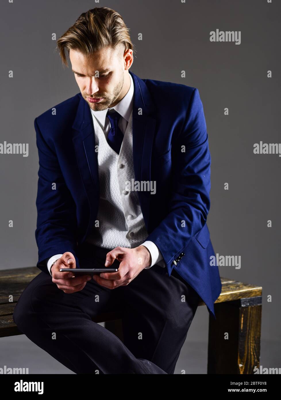 Man checking economic markers on his gadget. Man in classic suit or  businessman on dark background. Businessman with busy face in formal wear  hold smartphone. Business and technologies concept Stock Photo -