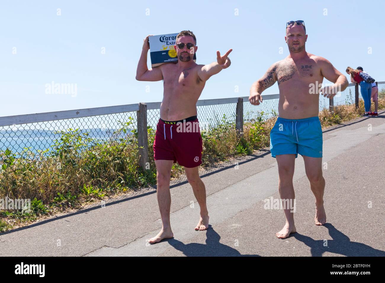 Bournemouth, Dorset UK. 25th May 2020. UK weather: scorching hot at Bournemouth beaches with clear blue skies and unbroken sunshine, as temperatures soar on Bank Holiday Monday. Sunseekers flock to the seaside and beaches are packed, with car parks full and cars left anywhere and everywhere. Ben and John head down to the beach with their supplies - a box of Corona! Credit: Carolyn Jenkins/Alamy Live News Stock Photo