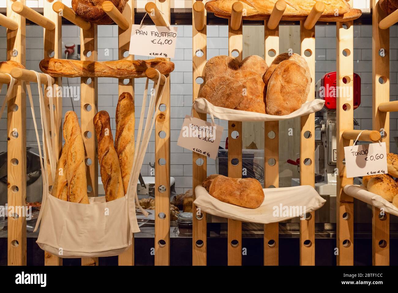 Inside view of an italian bakery shop with the kitchen in background and different bread types: pan fruttato (fruity bread), ciabatta (ciabatta bread) Stock Photo