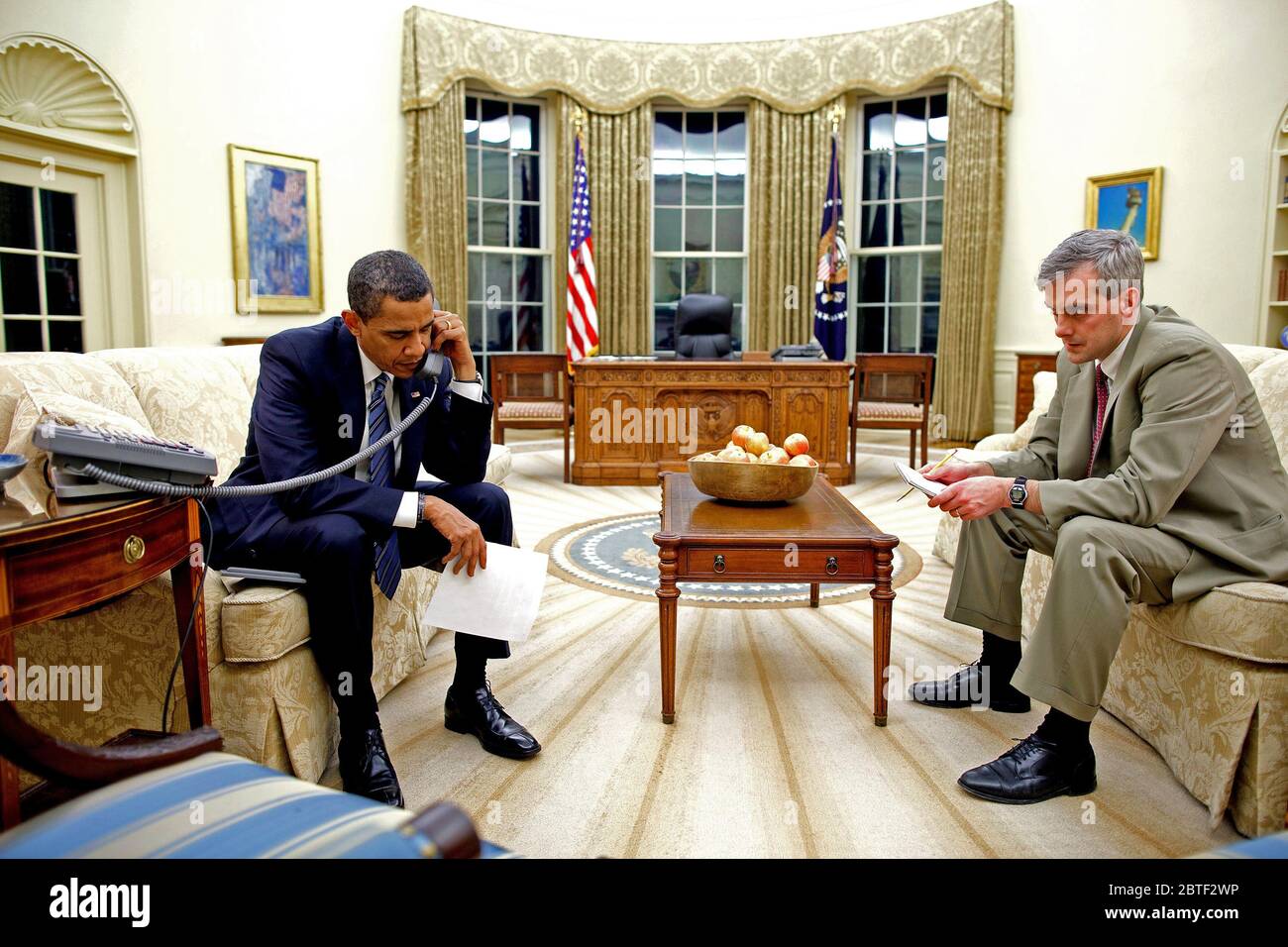 President Barack Obama speaks by phone with Arkansas Governor Mike Beebe regarding severe weather conditions in Arkansas, while  Denis McDonough, Director of Strategic Communications, National Security Council, NSC sits with him in the Oval Office 1/28/09. Stock Photo