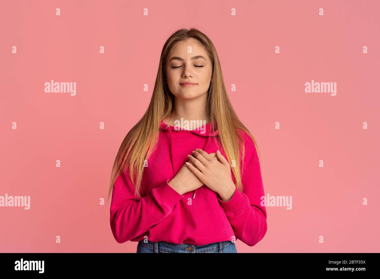 Cute girl tenager with closed eyes presses her hands to heart Stock Photo