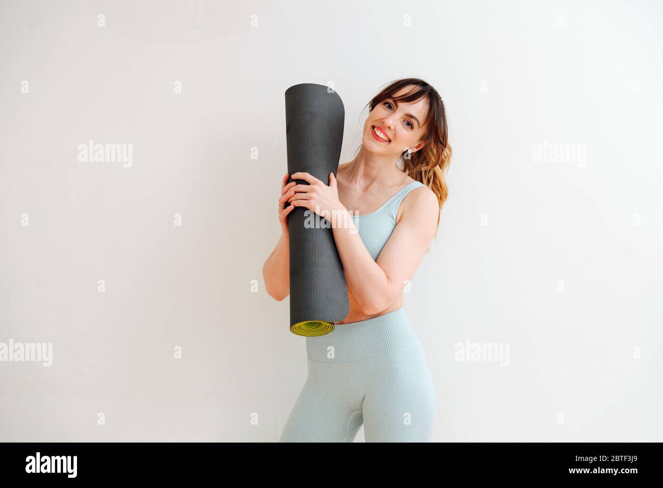 Portrait of a beautiful skinny girl in a sweatsuit holding a rolled-up mat Stock Photo