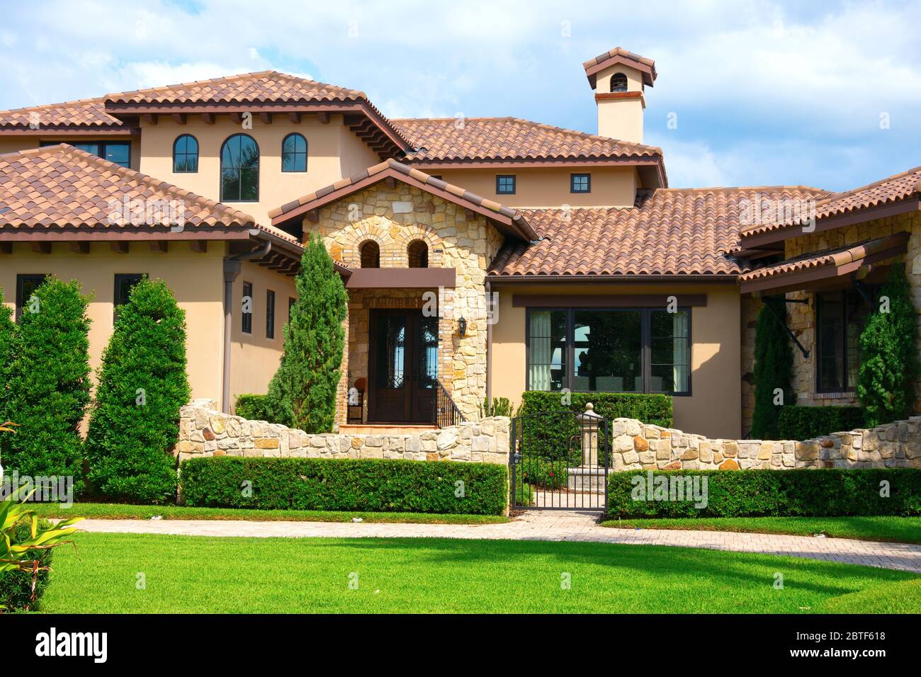 Beautiful Spanish style house exterior with natural rock facing and veneer siding and an impeccably maintained lawn and landscaping. Stock Photo