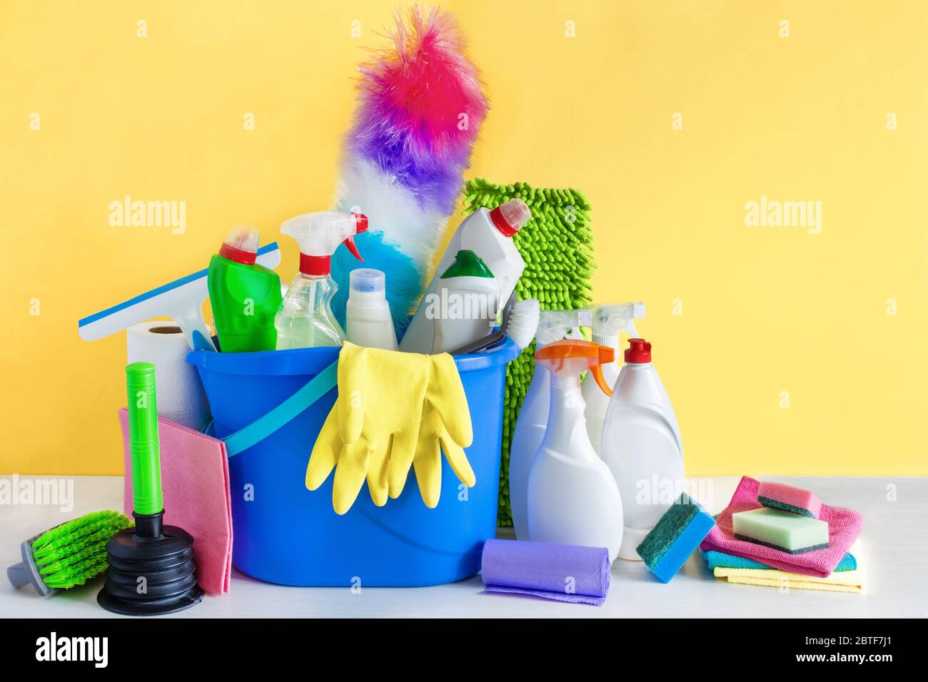 Bucket with bottles of detergent and cleaning tools over yellow