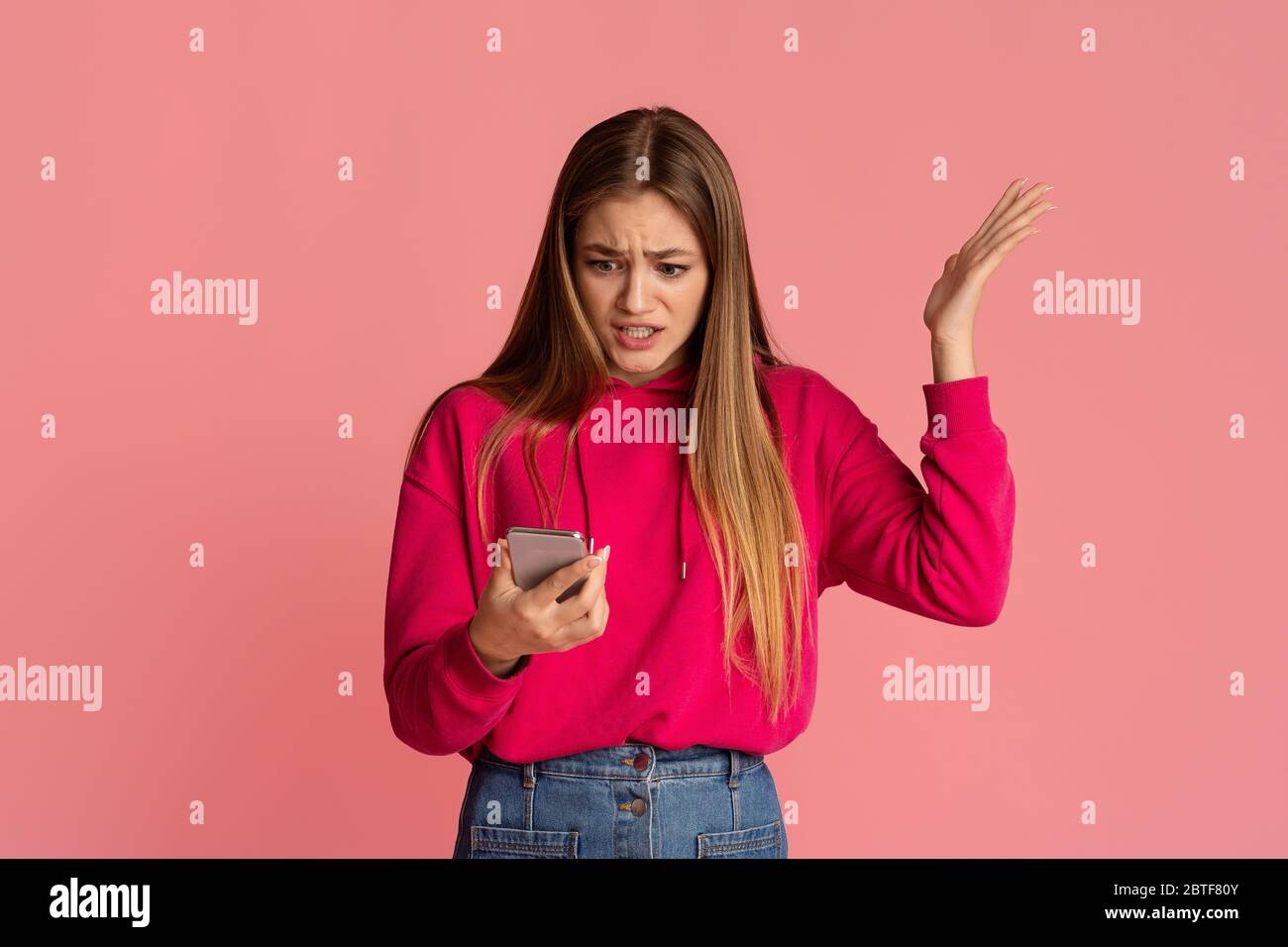 Discontent and indignation. Girl looks at smartphone and picks up hand Stock Photo