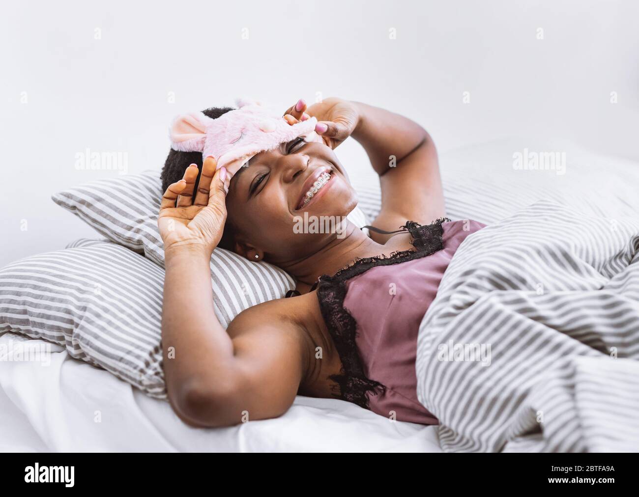 Smiling african american woman woke up, removes mask for sleeping Stock Photo
