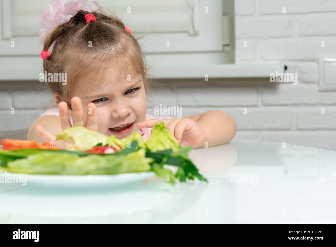 a little girl emotionally pushes away a plate of offered vegetables. children refuse vegetables in favor of junk food Stock Photo