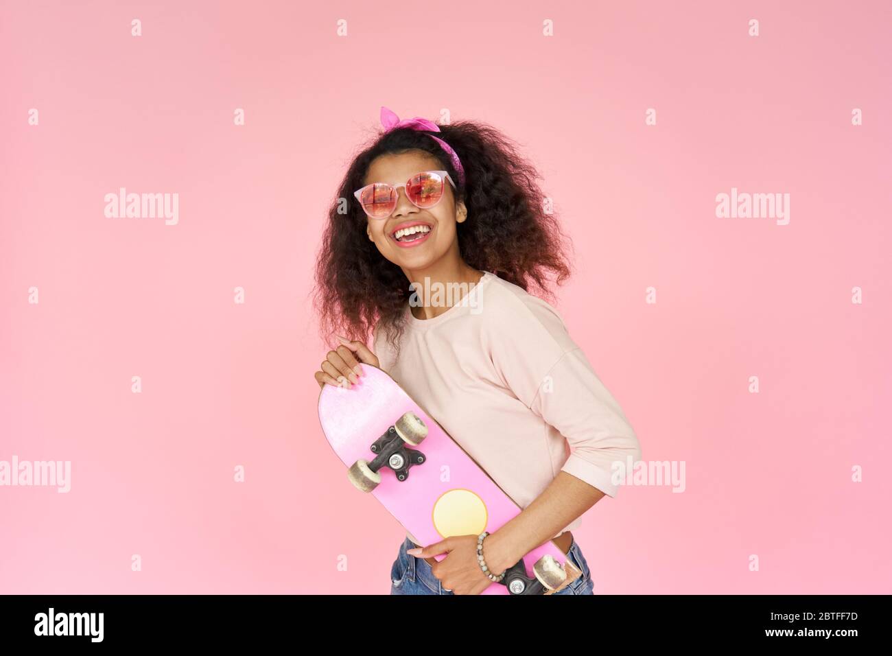 Happy african teen hipster girl hold skateboard isolated on pink background. Stock Photo