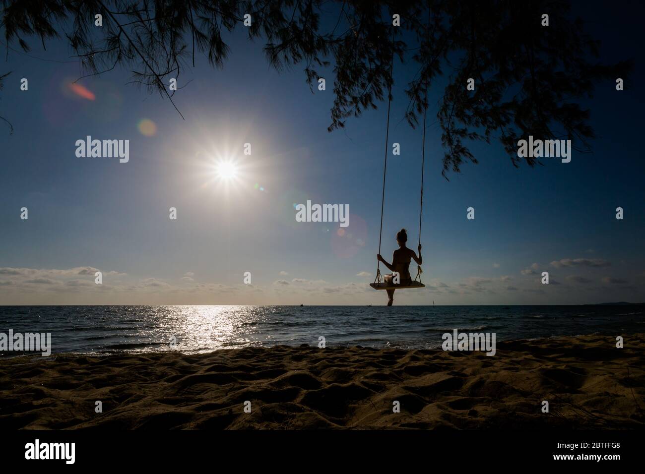 Siluette of woman on swing on tropical island Phu Quoc in Vietnam. Tourist on Ong Lang, Cua Can beach during hot sunny day. Stock Photo