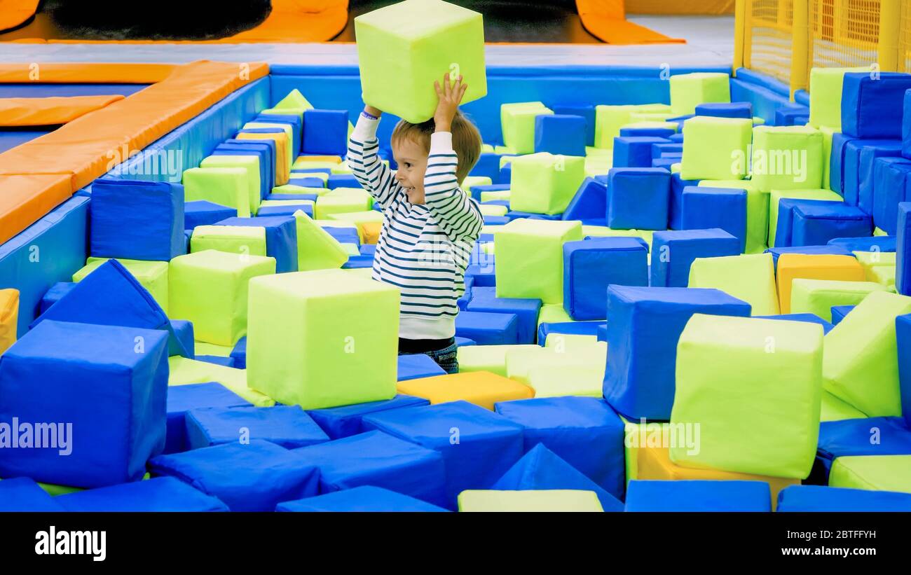 Happy smiling toddler boy playing and throwing soft cubes in big pit at ...