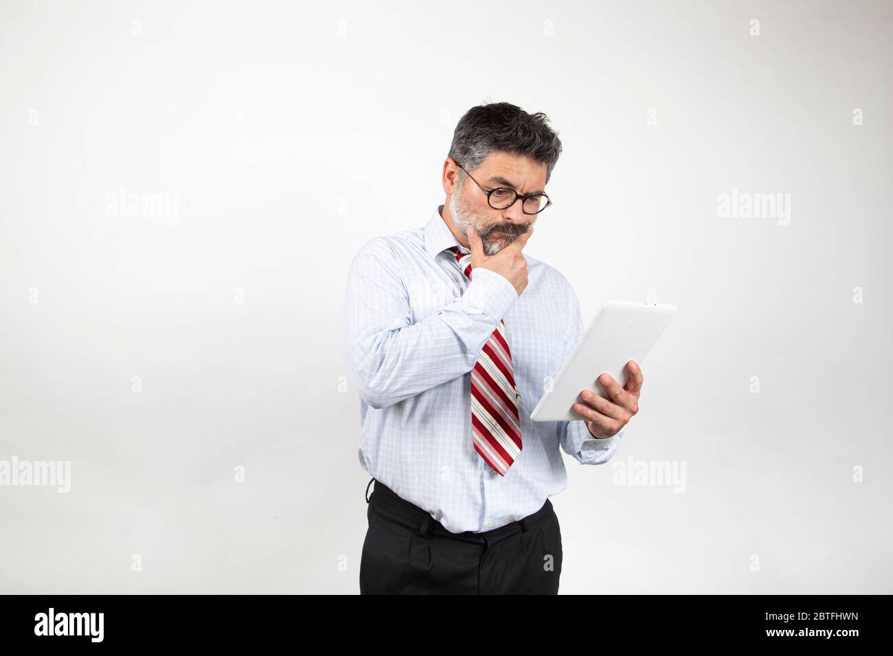 Portrait of classy serious Caucasian businessman in suit and glasses using tablet to read news on white background. Stock Photo