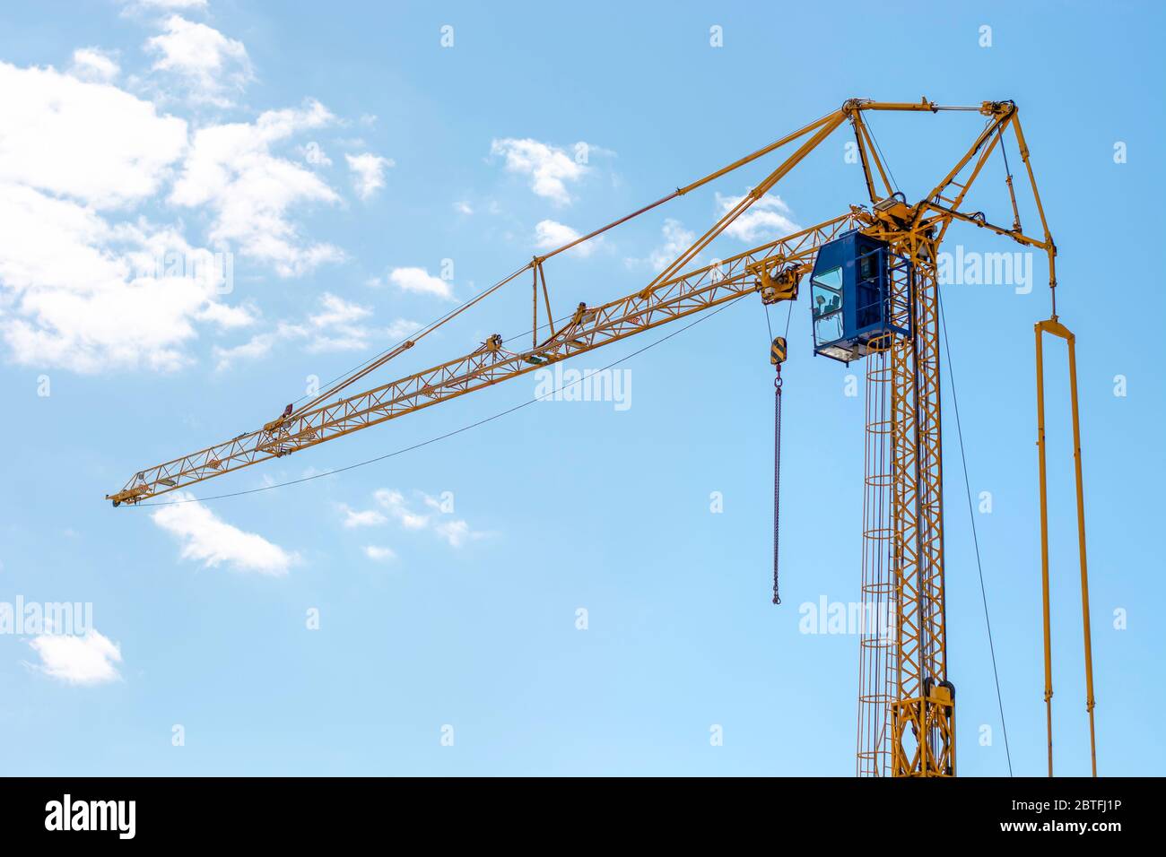 Industrial construction building crane. Yellow mobile rotary crane with a cabin of the operator against a blue sky. Large tall machine Stock Photo