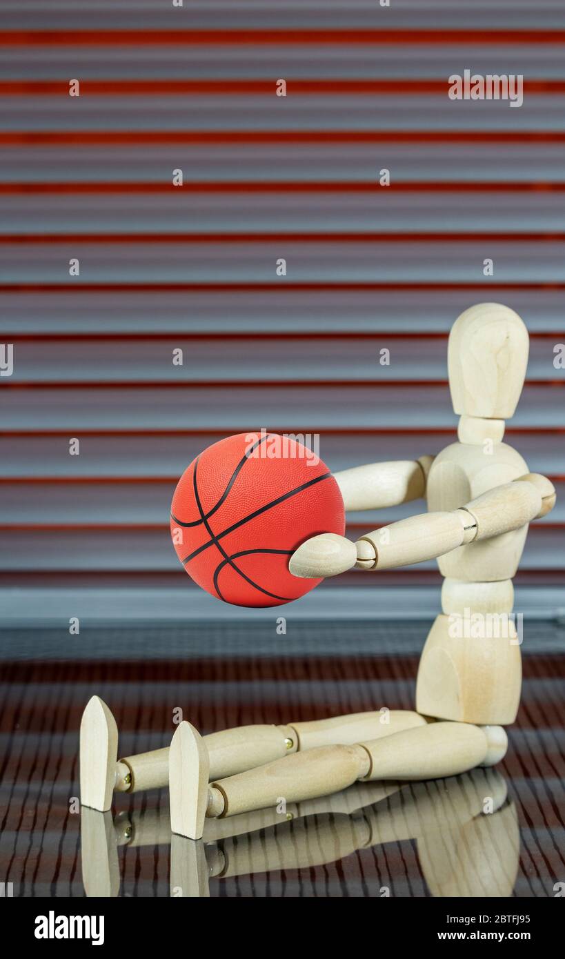 Wooden dummy with basketball in front of a jalousie plays with the ball Stock Photo