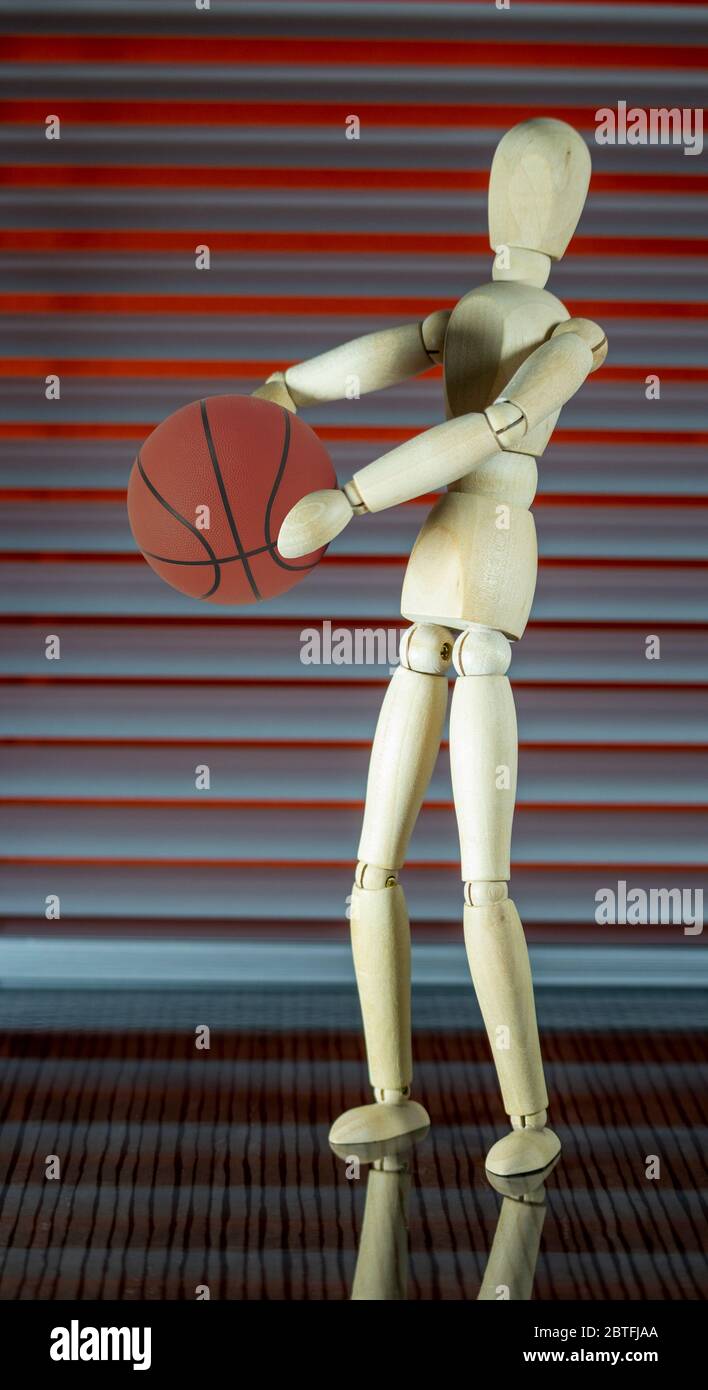 Wooden dummy with basketball in front of a jalousie plays with the ball Stock Photo