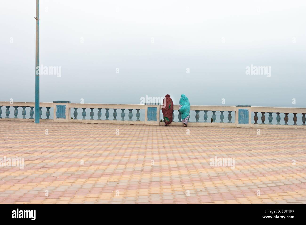 Two arabic woman with traditional clothing looking to the Atlantic Ocean at Sidi Ifni, Morocco Stock Photo