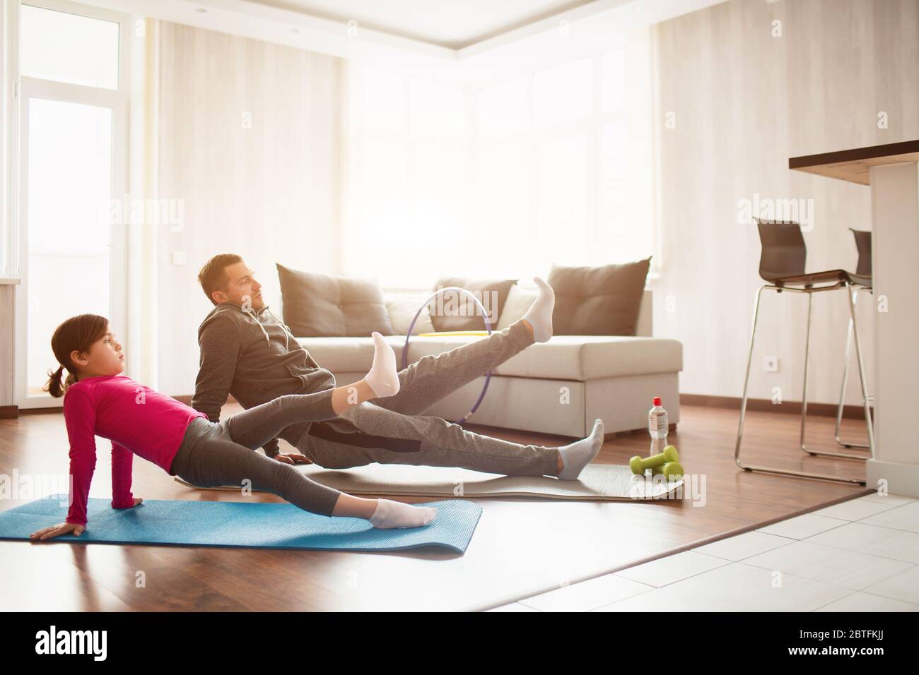 father and daughter are training at home. Workout in the apartment. Sports at home. Rreverce plank with leg raise on the floor at home. Stock Photo