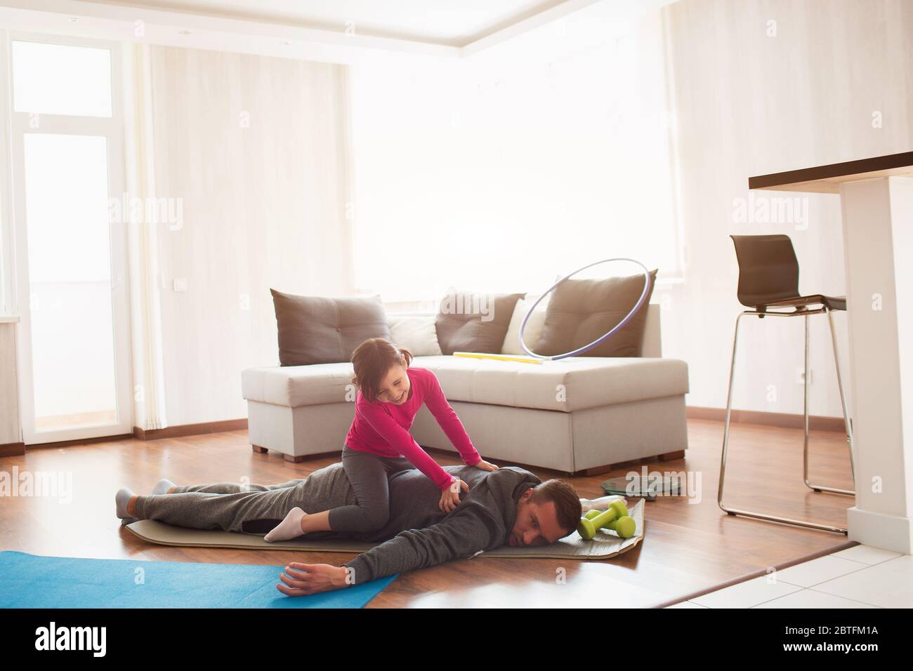 father and daughter are training at home. Workout in the apartment. Sports at home. Dad is very tired. Daughter climbed on her back and has fun Stock Photo