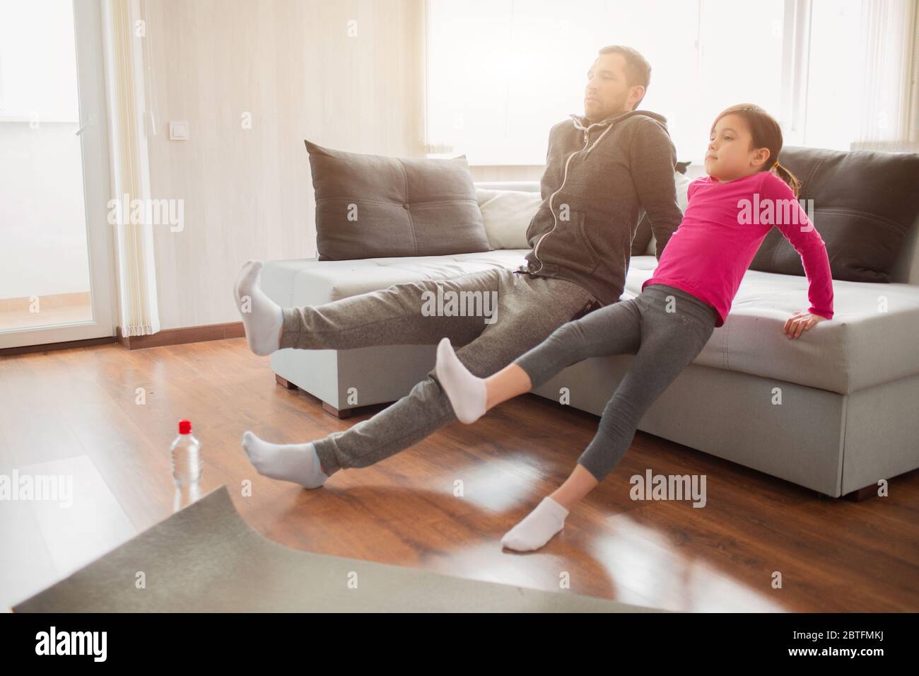 father and daughter are training at home. Workout in the apartment. Sports at home. Rreverce plank with leg raise on the floor at home. Stock Photo