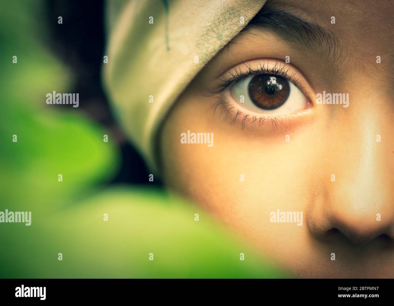 Macro view of a little girl hides behind a green leaf, warm colors, nature concept, soft and natural light Stock Photo