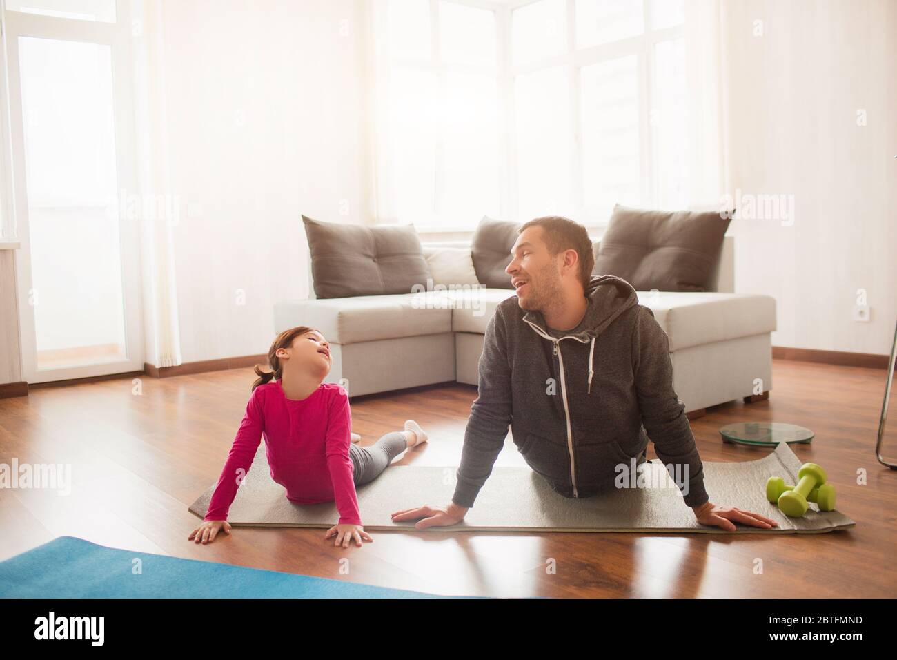 father and daughter are training at home. Workout in the apartment. Sports at home. They make faces and have fun on a yoga mat. Stock Photo