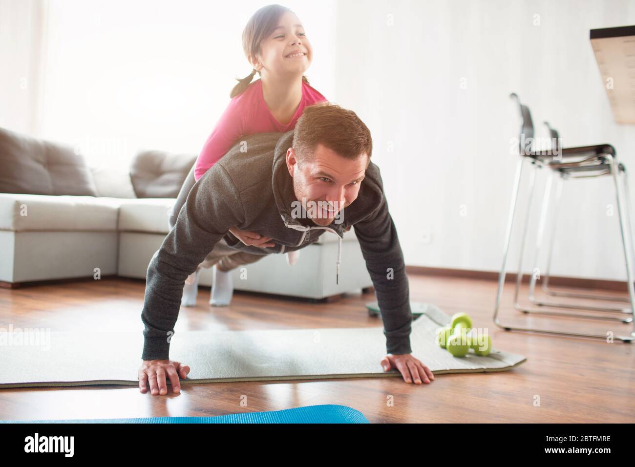 father and daughter are training at home. Workout in the apartment. Sports in home conditions. They make the doing plank. daughter climbed on dad. He Stock Photo