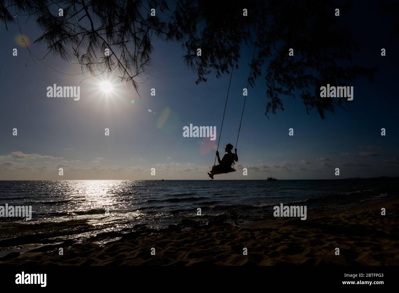Siluette of man on swing on tropical island Phu Quoc in Vietnam. Tourist on Ong Lang, Cua Can beach during hot sunny day. Stock Photo