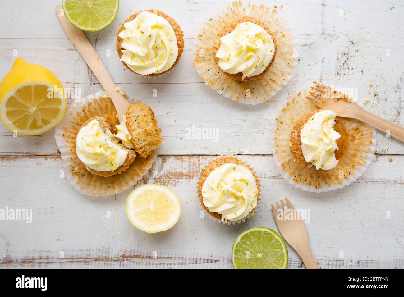 Lemon and poppy seed cupcakes with cheese cream frosting and lemon and lime zest on a rustic white wooden table. Top view Stock Photo