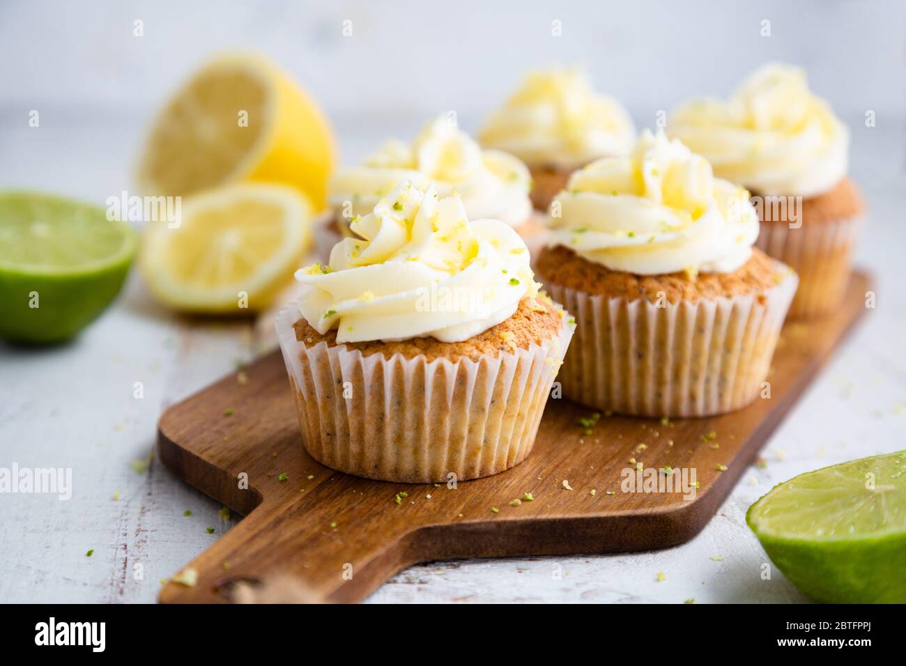 Lemon and poppy seed cupcakes with cheese cream frosting and lemon and lime zest on a cutting board Stock Photo