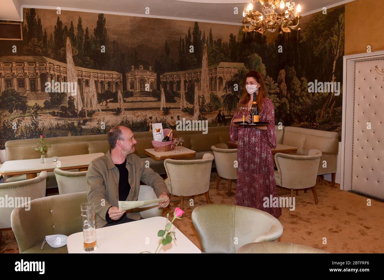 Munich, Germany. 25th May, 2020. The gastronome Martina Grandjean (r) serves the guest Andreas Keck (l) a champagne with mouth protection in the Cafe Jasmin. As of today the interiors of the restaurants in the Free State are open again. Credit: Felix Hörhager/dpa/Alamy Live News Stock Photo