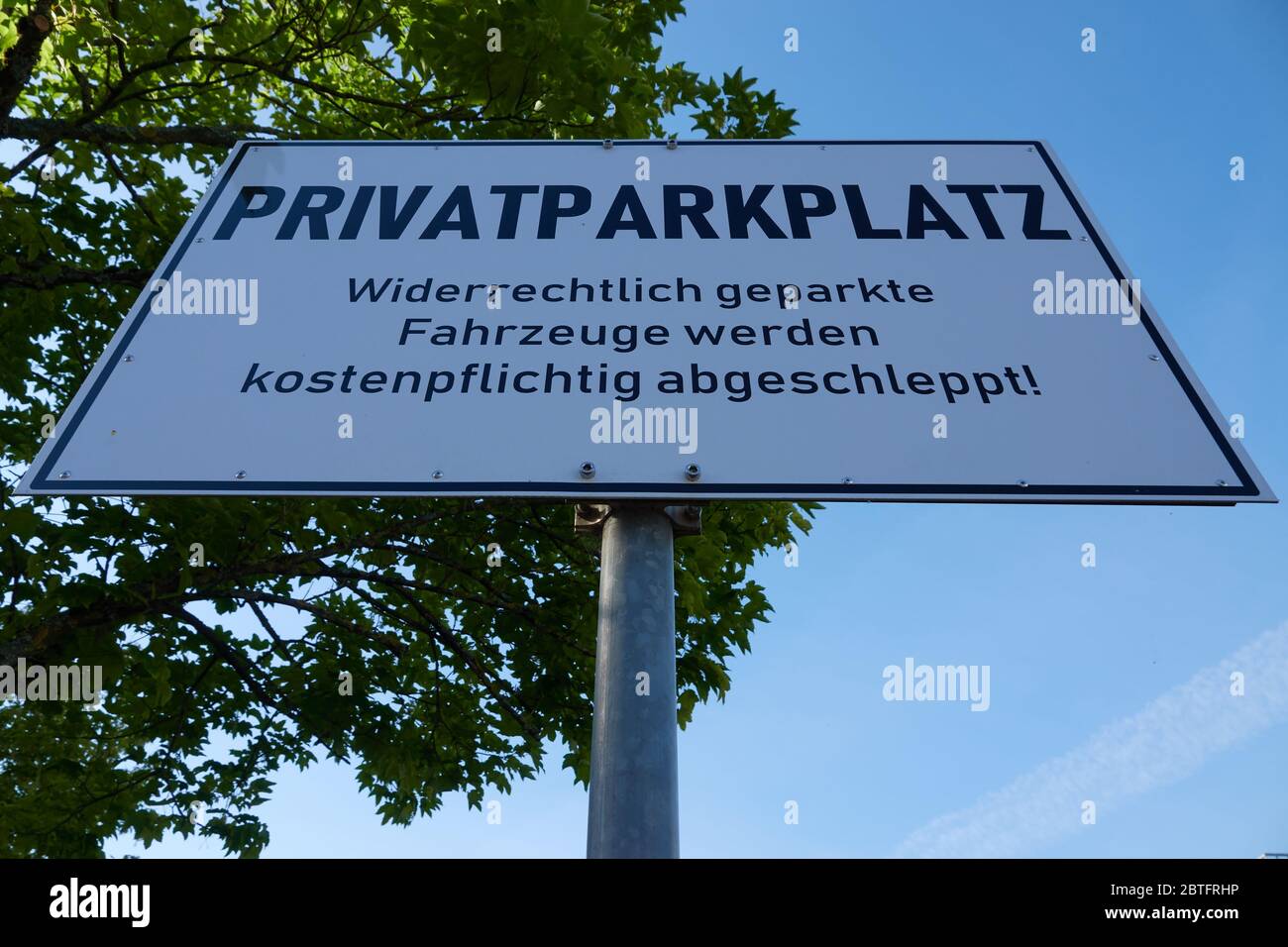 White rectangular sign: private parking ( translation of german word Privatparkplatz: private parking) in front of green tree and sky blue deep perspe Stock Photo