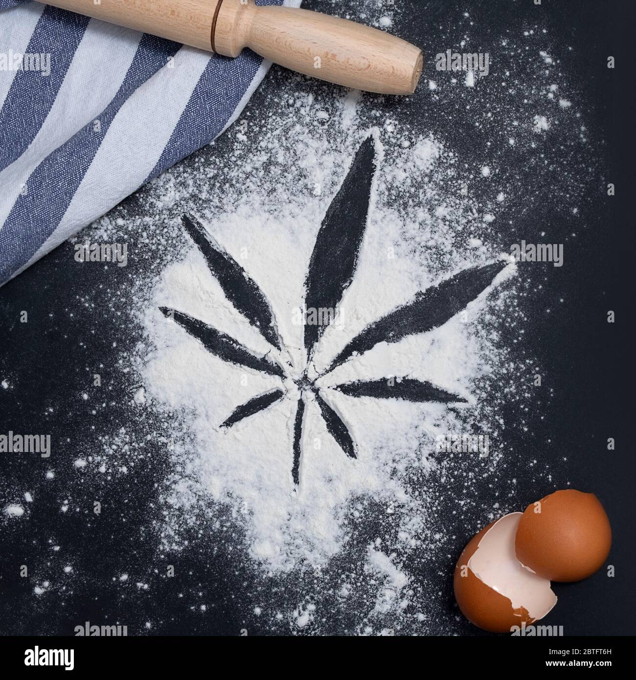 Cannabis recipes or cannabis baking concept. Top view of cannabis leaf made from flour with egg shells and wooden rolling pin Stock Photo