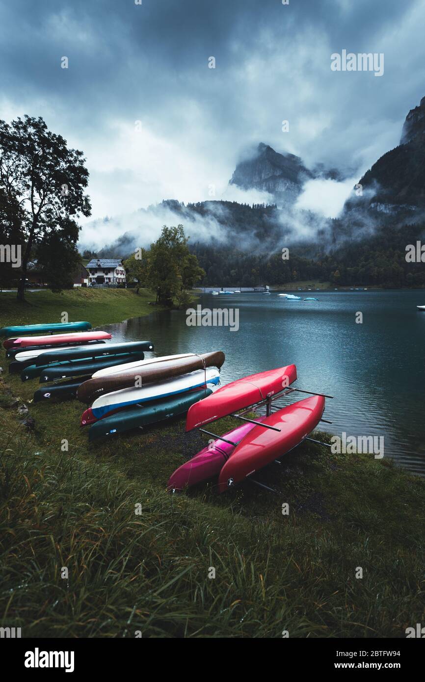 Beautiful colourful boats and kayaks on the lake. Kayaking photo concept with clear azure water and dark green grass. Moody weather with foggy mountai Stock Photo
