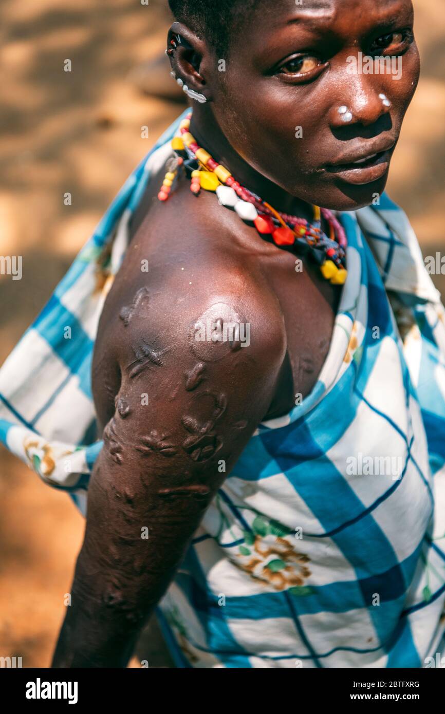 BOYA TRIBE, SOUTH SUDAN - MARCH 10, 2020: Woman in traditional colorful accessories and checkered cloth with ritual piercing and scars looking at Stock Photo