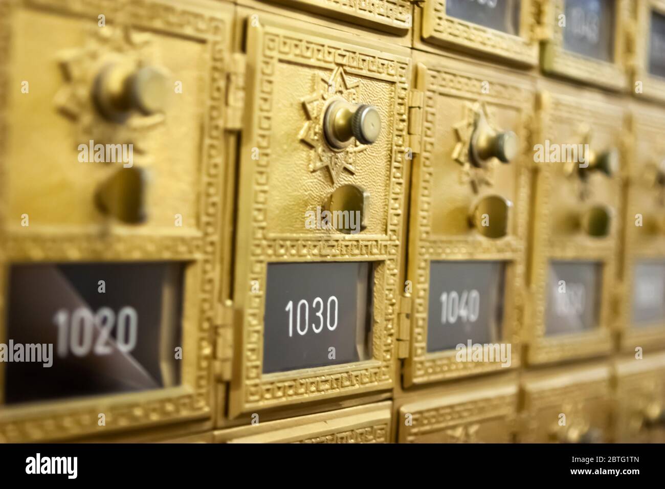 Row of vintage brass pigeonhole mailboxes with doors and combination locks in a mail room Stock