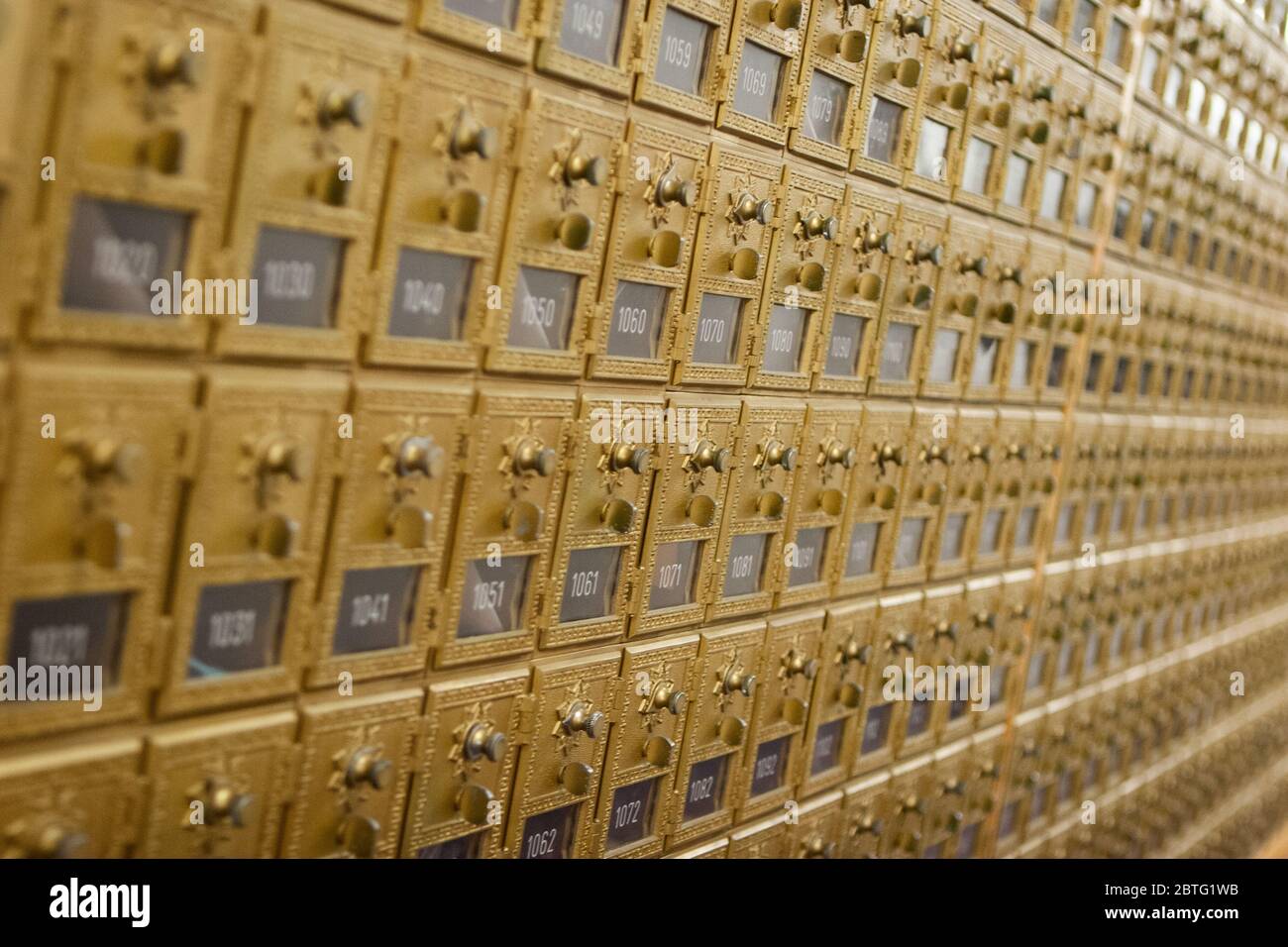 Row of vintage brass pigeonhole mailboxes with doors and combination locks in a mail room Stock