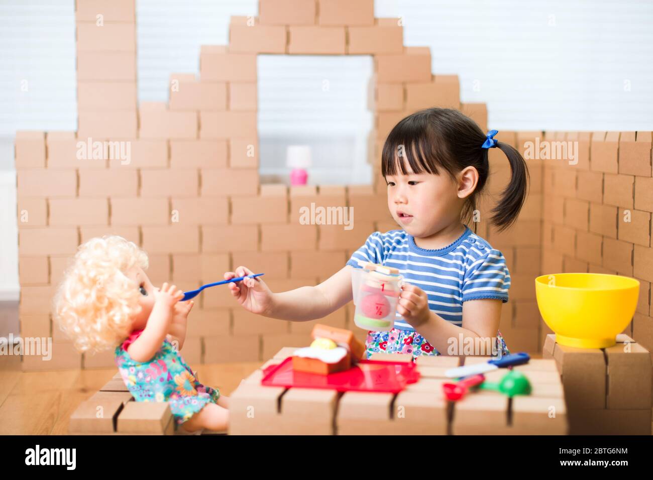toddler girl pretend play baby care in a cardboard block house Stock