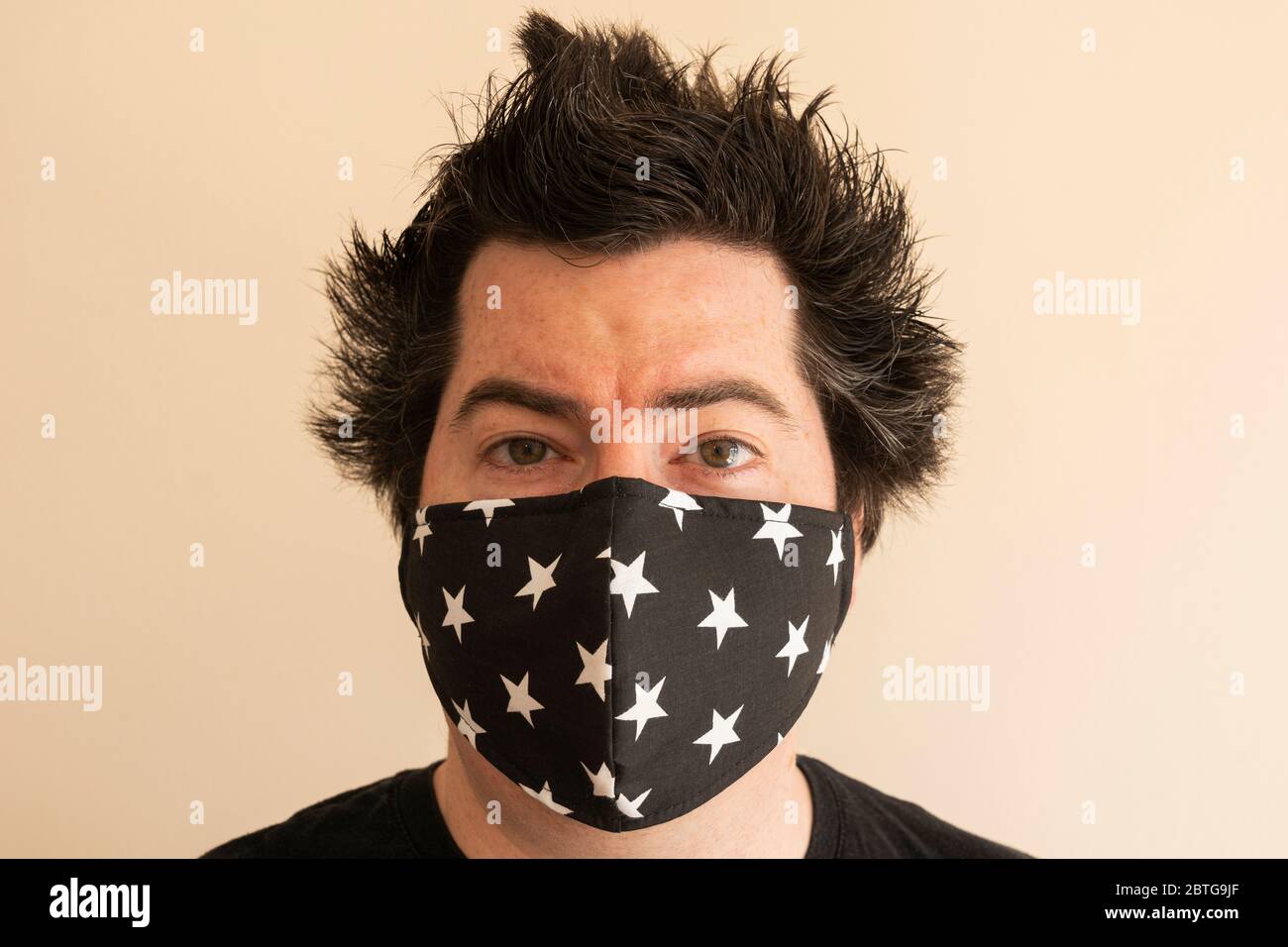 A man in his late thirties with a reusable face mask looking directly at the viewer during the Covid 19 Coronavirus pandemic with crazy lockdown hair Stock Photo
