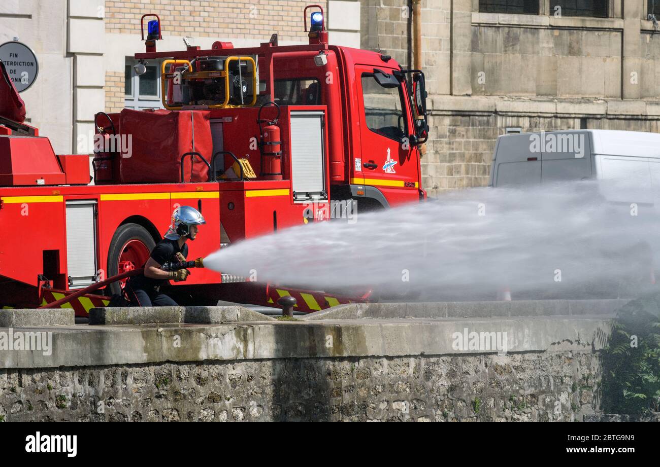 French firefighters training drill using a fire hose to spray high pressure water in front a red fire engine truck parked along the Canal de l'Ourcq. Stock Photo
