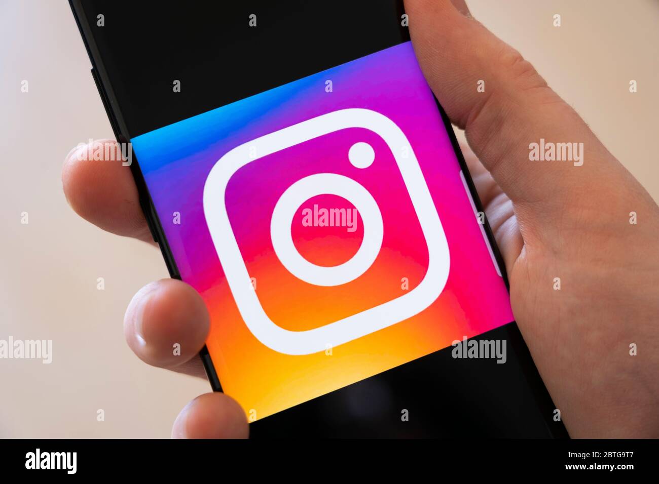 A man's hand holding a smartphone displaying a large logo for the photo sharing social media app Instagram Stock Photo