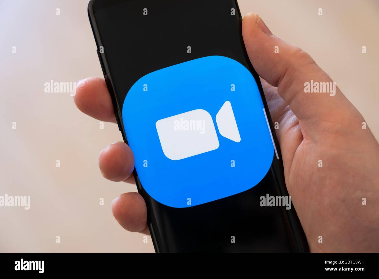 A man's hand (man is 39) holding a smartphone displaying a large logo for the video calling app Zoom Stock Photo