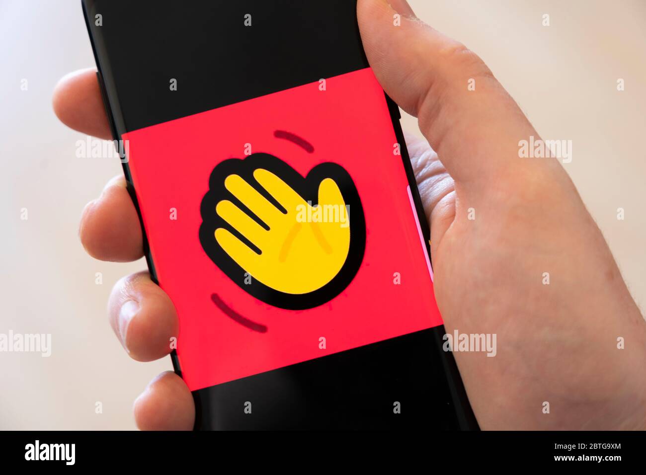 A man's hand holding a smartphone displaying a large logo for the video calling app Houseparty Stock Photo