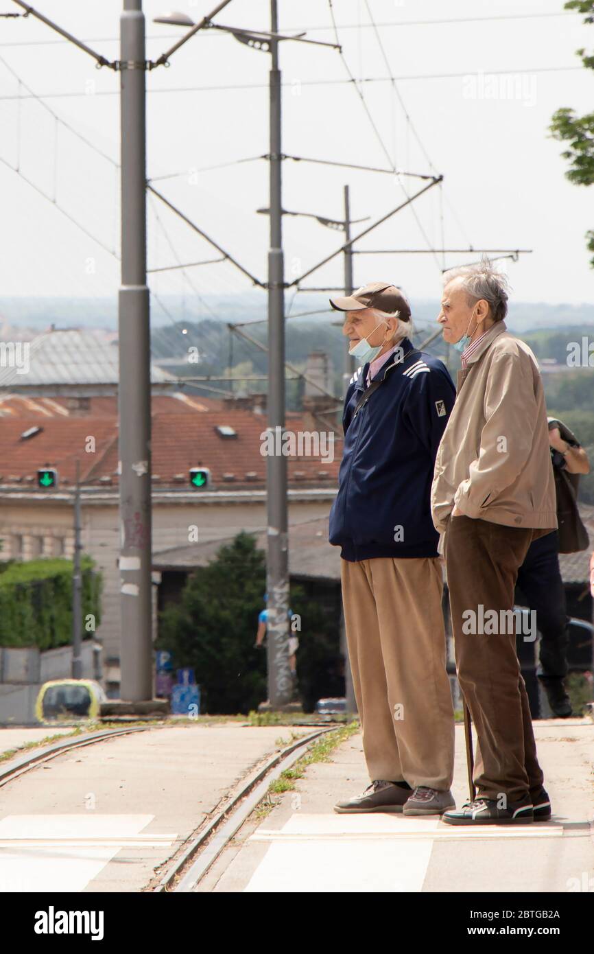 Belgrade, Serbia - May 21, 2020: Two senior men wearing face surgical masks standing at zebra crossing next to a tram road Stock Photo