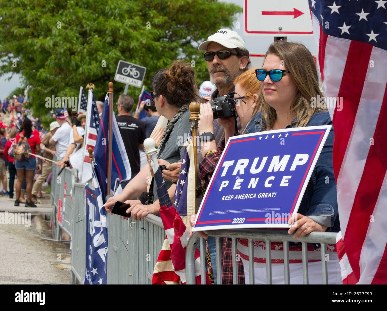 Baltimore, Maryland, USA. 25th May, 2020. Woman wearing mirrored sunglasses among crowd behind barricades holds sign reading 'Trump, Pence, Keep America Great 2020' while another Trump supporter's American flag is draped behind her, outside historic Fort McHenry in Baltimore, Maryland; where President Donald Trump and First Lady Melania Trump visit on Memorial Day 2020 despite urging from Baltimore Mayor Bernard C. “Jack” Young to cancel to avoid setting a bad example while the city remains under a stay-at-home order (with exemptions including some outdoor exercise). Kay Howell/Alamy Live News Stock Photo