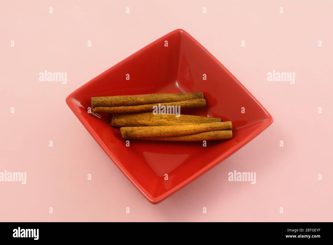 Cinnamon sticks spice in red square bowl on pink background Stock Photo