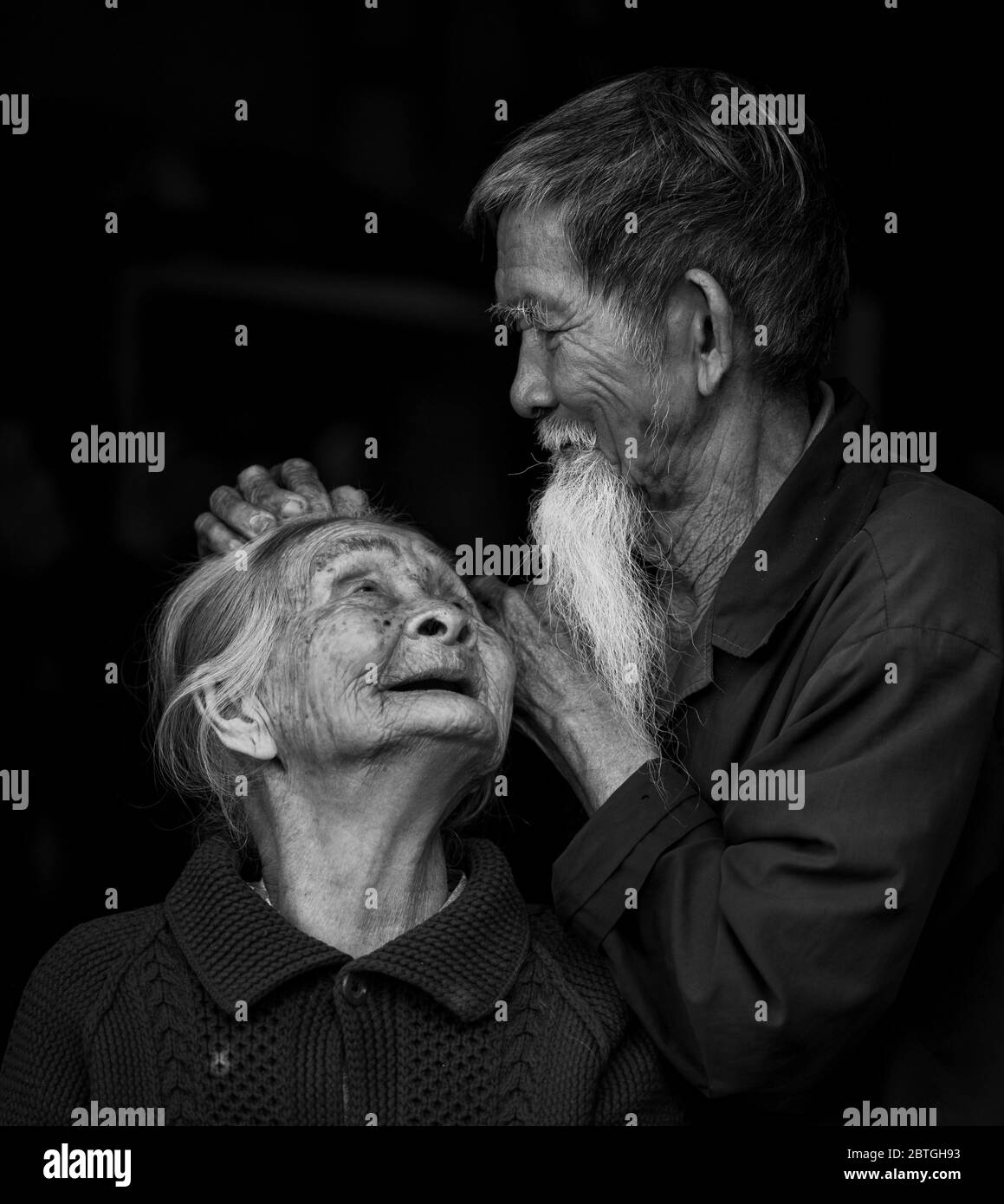 HOI AN - MAR 10, 2018: An old man gently fixing his wife's hair in a black background in Hoi An, Vietnam on on 10 March 2018 Stock Photo